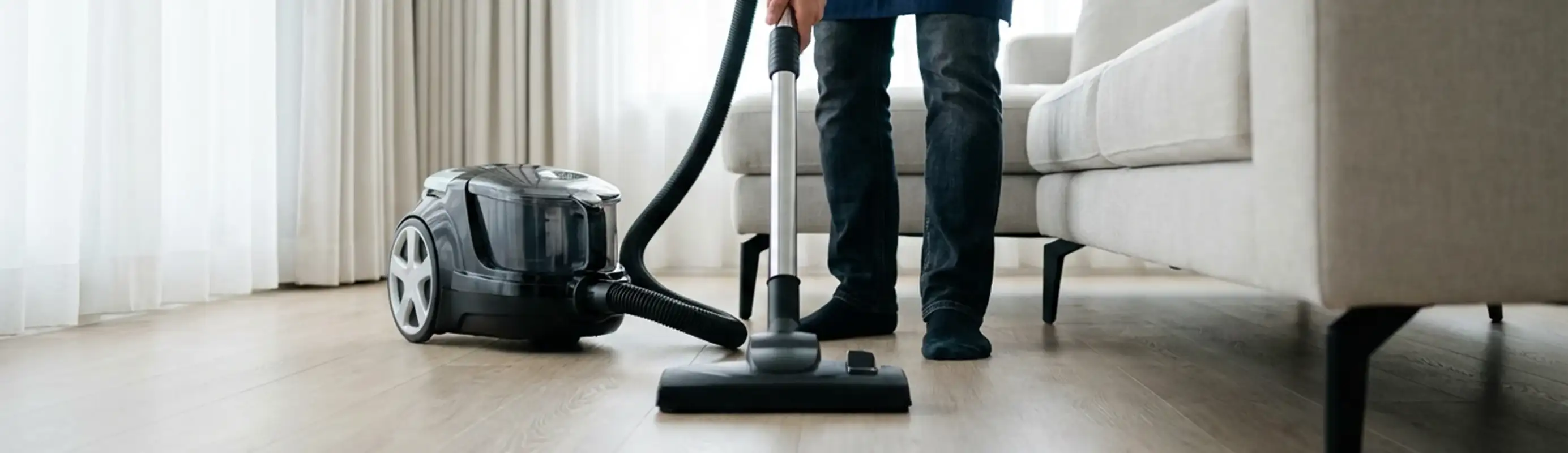Professional house cleaner vacuuming a living room floor with a canister vacuum cleaner, Raleigh, NC.