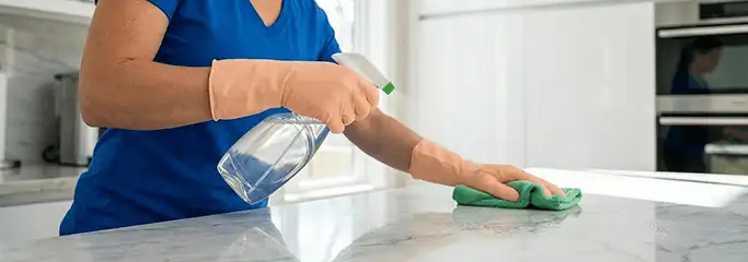 Maid service worker spraying and wiping a kitchen countertop with a microfiber cloth for sanitizing, Raleigh, NC.