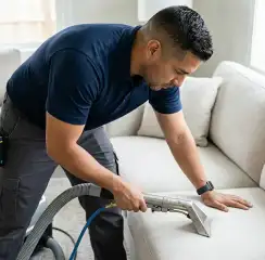 Professional upholstery cleaning technician using an extraction wand to deep-clean a fabric sofa, Raleigh, NC.