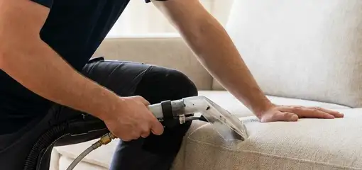 Professional upholstery cleaner deep-cleaning a fabric sofa with a handheld extraction tool, Raleigh, NC.
