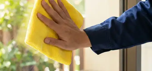 House cleaner wiping a glass window with a yellow microfiber cloth for streak-free cleaning, Raleigh, NC.